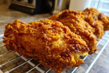 Close-up of several pieces of golden brown, extra-crispy fried chicken resting on a wire cooling rack.