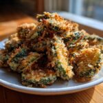 A pile of golden brown, crispy Fried Pickles with thick breading served on a small white plate.
