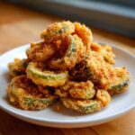 A close-up of a pile of golden-brown, crispy Fried Pickles served on a white plate.