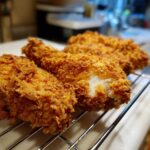 Close-up of perfectly golden brown fried chicken resting on a wire rack, showing the crispy coating.