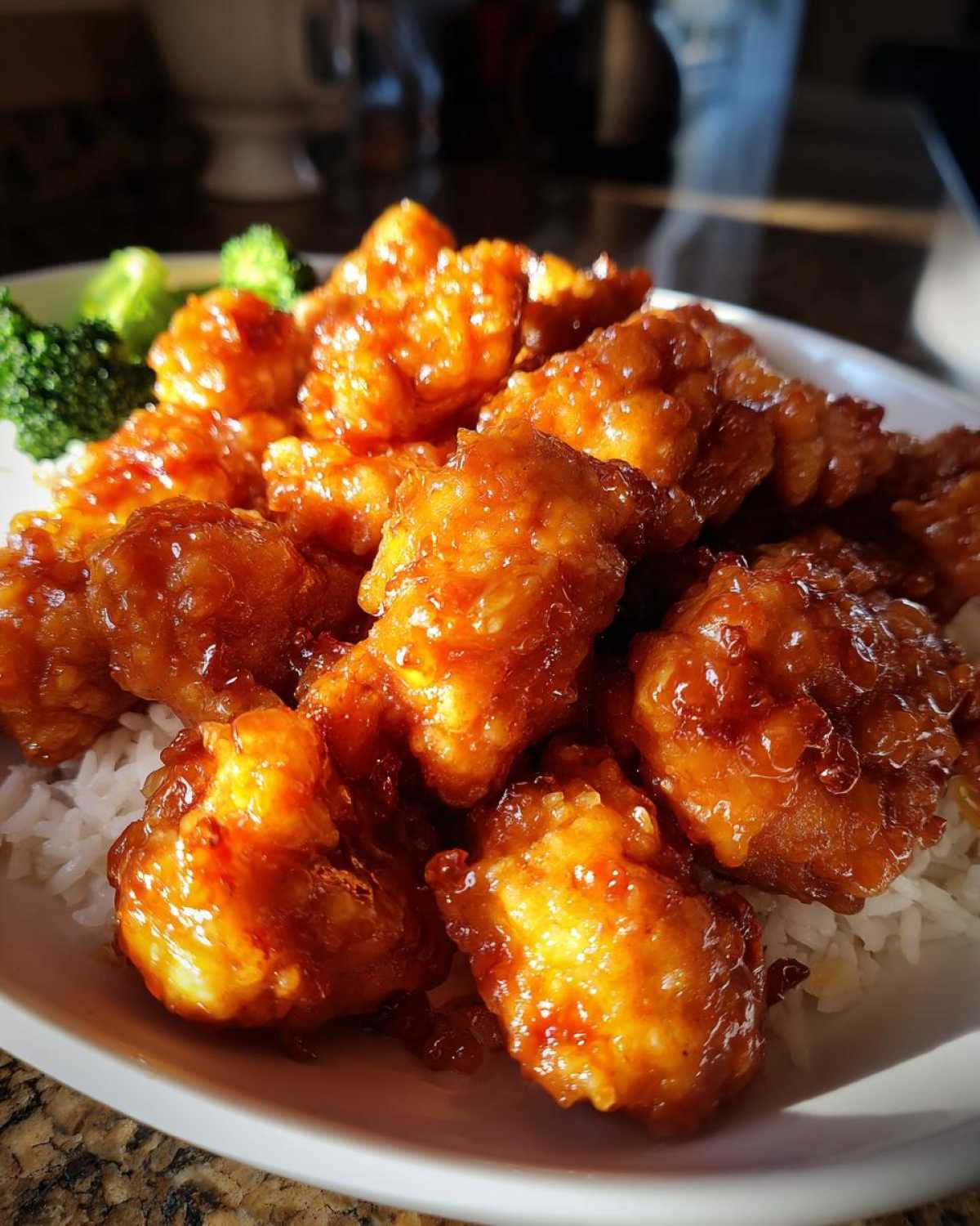 Close-up of crispy orange chicken pieces coated in glossy sauce, served over white rice with a side of steamed broccoli.