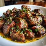 Close-up of tender crockpot steak bites coated in a glossy garlic butter sauce and fresh parsley.