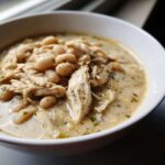 Close-up of a white bowl filled with creamy crockpot white chicken chili, featuring shredded chicken and white beans.