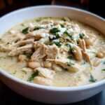 Close-up of a bowl of creamy crockpot white chicken chili topped with shredded chicken, white beans, and feta cheese.