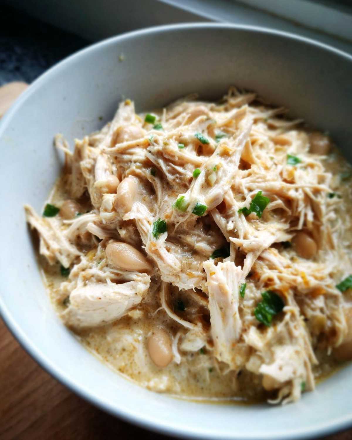 Close-up of a bowl filled with shredded chicken, white beans, and creamy sauce from the crockpot white chicken chili.