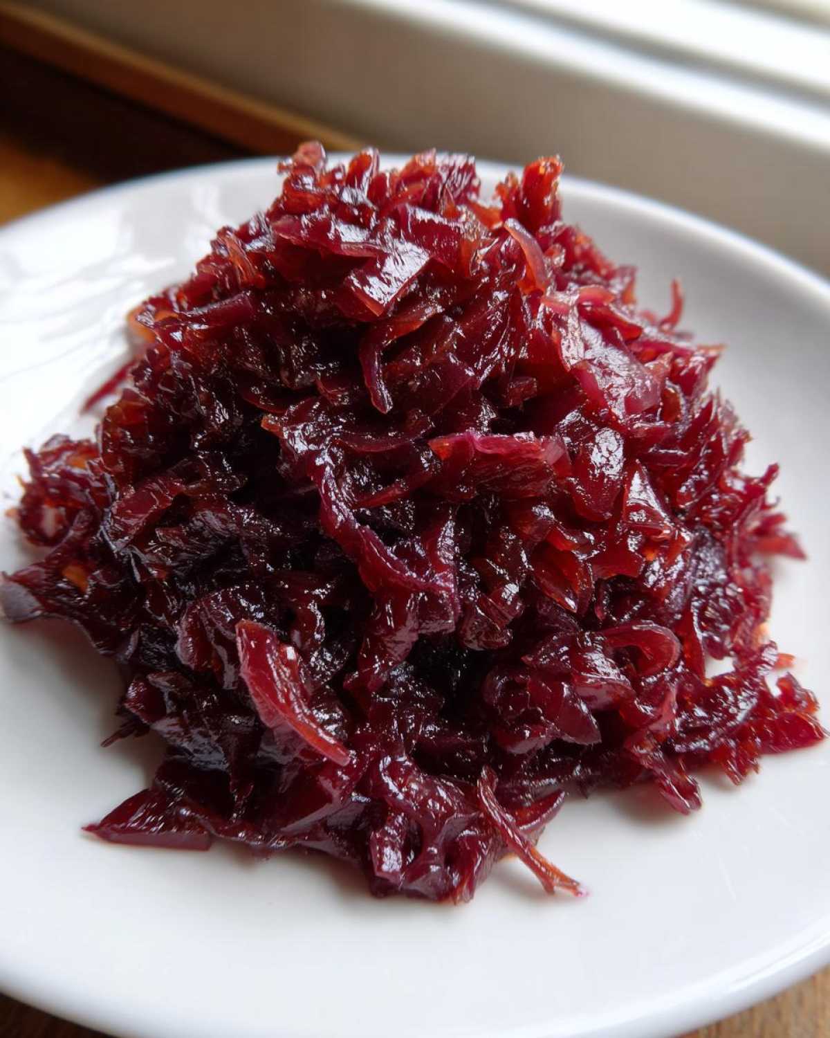 A close-up of deeply rich, dark red caramelized onions piled high on a small white plate.