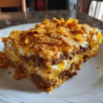 A thick slice of Dorito Casserole layered with seasoned ground beef, creamy sauce, and topped with melted cheese and crushed Doritos.