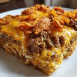 Close-up of a square serving of Dorito Casserole topped with melted cheese and crushed chips.