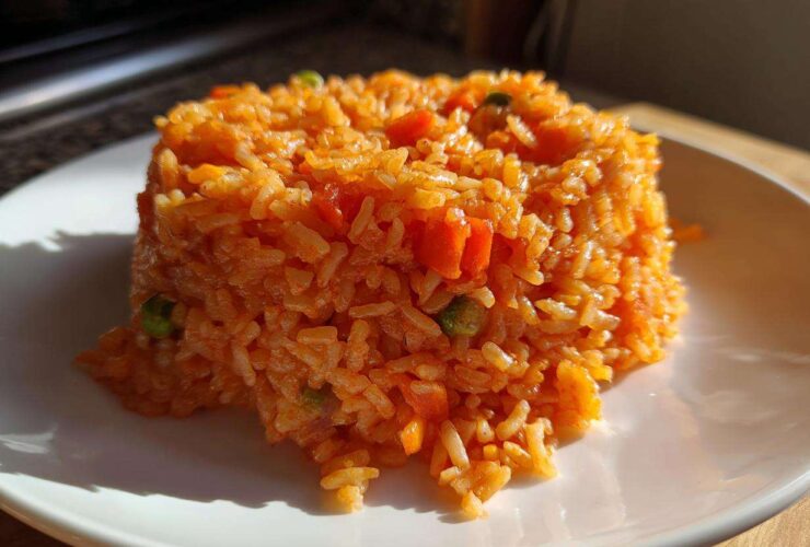 A serving of bright orange Spanish rice, molded into a neat mound on a white plate, showing visible pieces of carrots and peas.