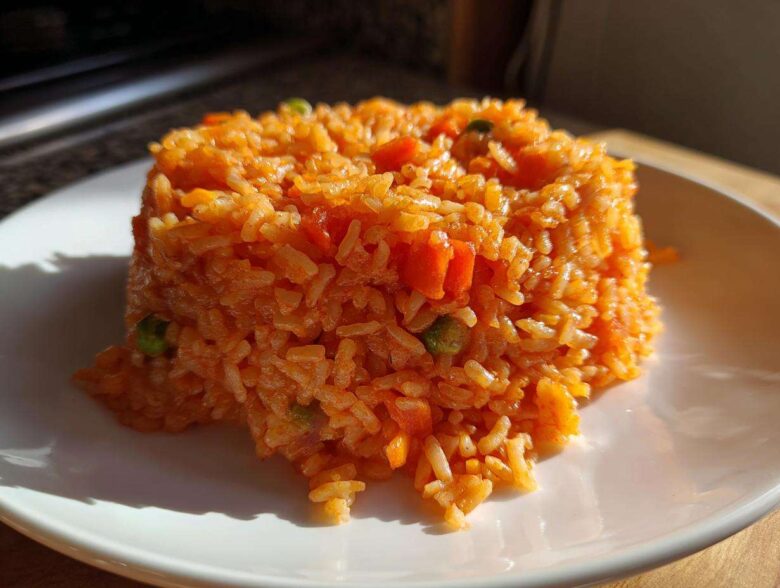 A serving of bright orange Spanish rice, molded into a neat mound on a white plate, showing visible pieces of carrots and peas.