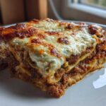 A thick, layered slice of zucchini lasagna featuring rich meat sauce and a bubbly, browned cheese topping.