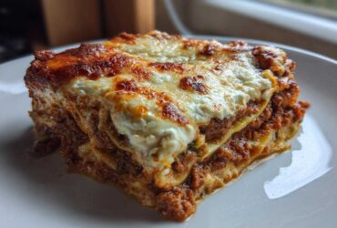 A thick, layered slice of zucchini lasagna featuring rich meat sauce and a bubbly, browned cheese topping.