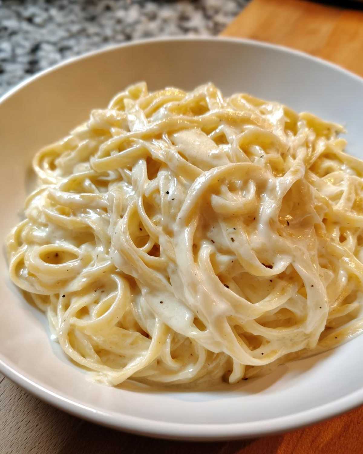 Close-up of fettuccine pasta coated generously in rich, creamy homemade alfredo sauce with black pepper specks.