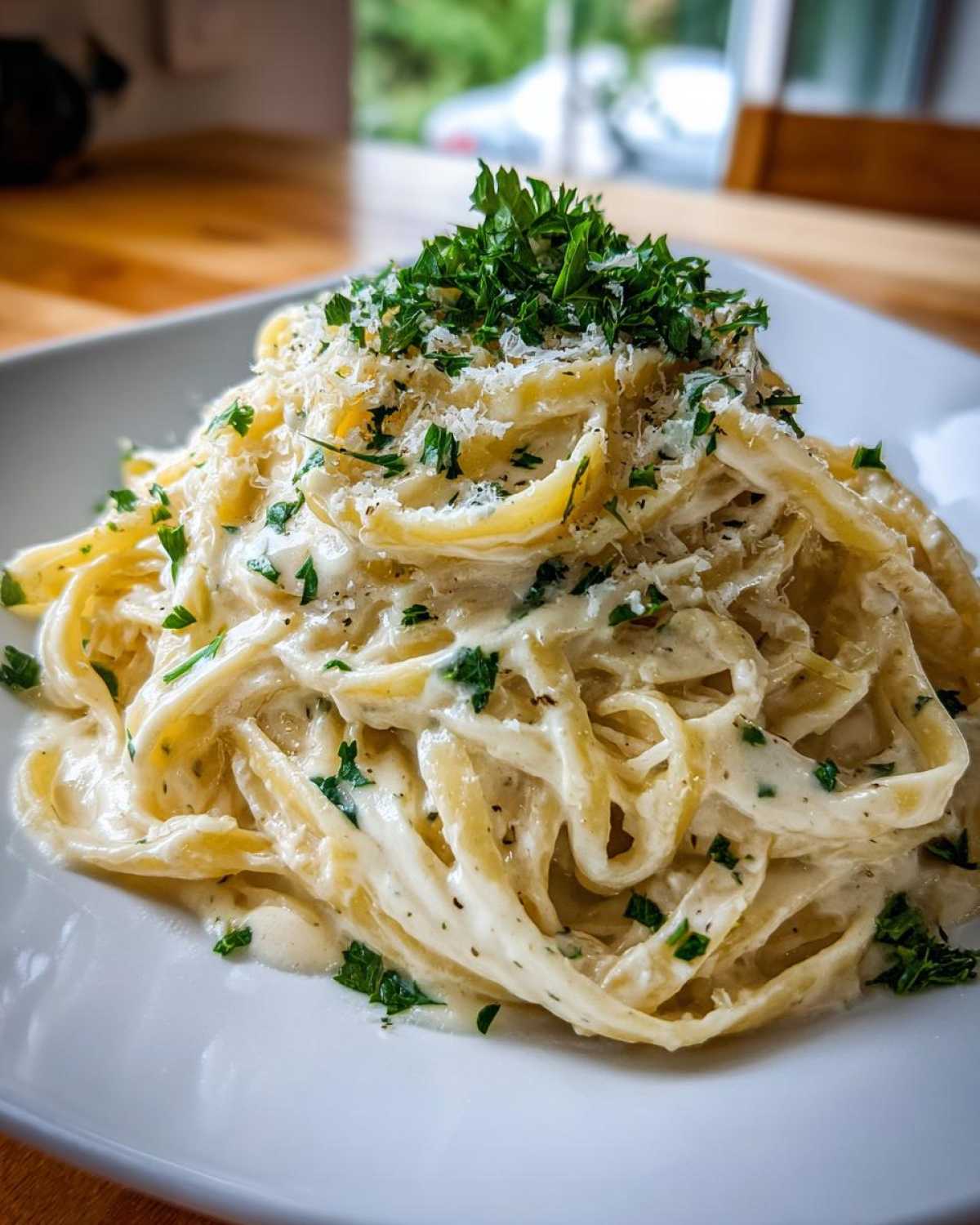 Close-up of fettuccine pasta generously coated in creamy homemade alfredo sauce, topped with Parmesan and fresh parsley.