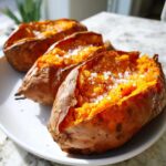 Three fluffy baked sweet potato halves topped with coarse sea salt on a white plate.