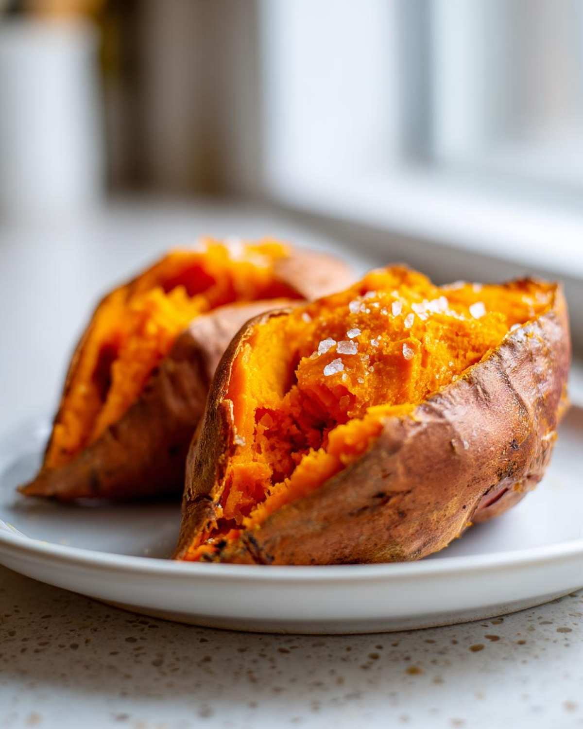 Two halves of a fluffy baked sweet potato sprinkled with coarse sea salt on a white plate.