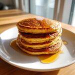 A tall stack of four fluffy greek yogurt pancakes drizzled generously with golden syrup on a white plate.