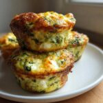 A stack of three golden-brown muffin tin egg bites with visible spinach and cheese, sitting on a white plate.