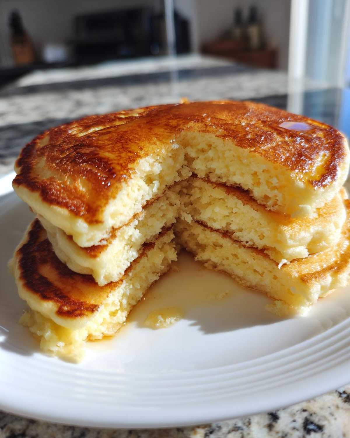 A stack of three fluffy pancakes cut in half, showing the airy interior and golden-brown tops, drizzled with syrup.