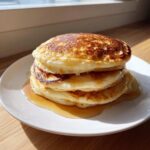A tall stack of three fluffy sourdough pancakes drizzled with maple syrup on a white plate.