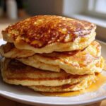 A tall stack of four fluffy sourdough pancakes drizzled generously with golden syrup on a white plate.