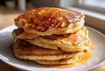 A tall stack of four fluffy sourdough pancakes drizzled generously with golden syrup on a white plate.