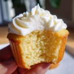 Close-up of a fluffy vanilla cupcakes with white frosting, showing the moist interior after a bite has been taken.