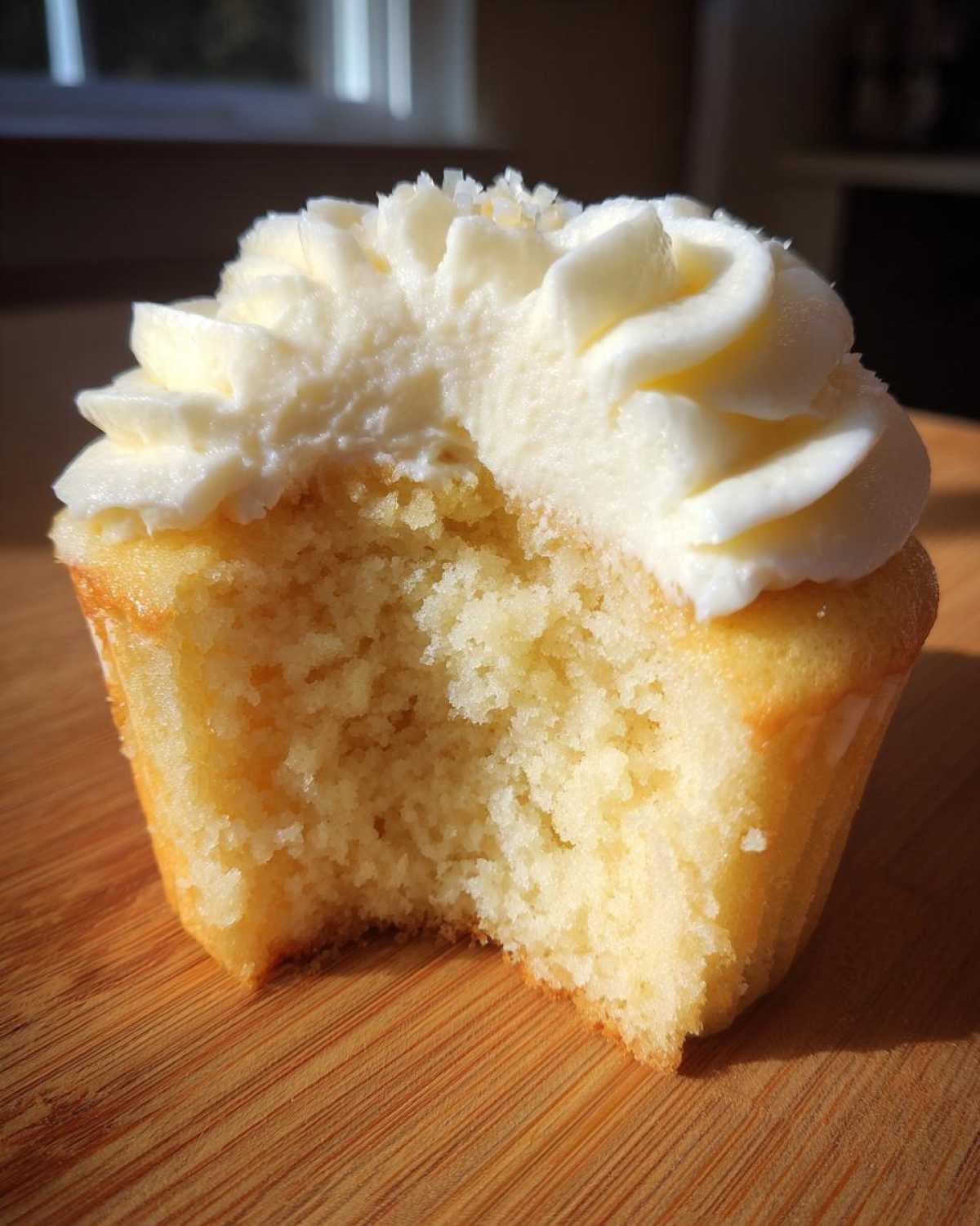 Close-up of a fluffy vanilla cupcakes with white frosting, showing a bite taken out revealing the moist crumb.
