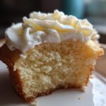 Close-up of a vanilla cupcakes half eaten, showing the fluffy interior and white buttercream frosting.