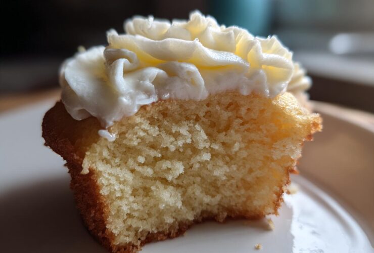 Close-up of a vanilla cupcakes half eaten, showing the fluffy interior and white buttercream frosting.