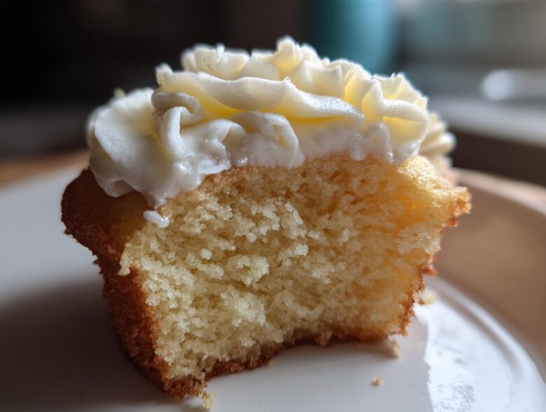 Close-up of a vanilla cupcakes half eaten, showing the fluffy interior and white buttercream frosting.