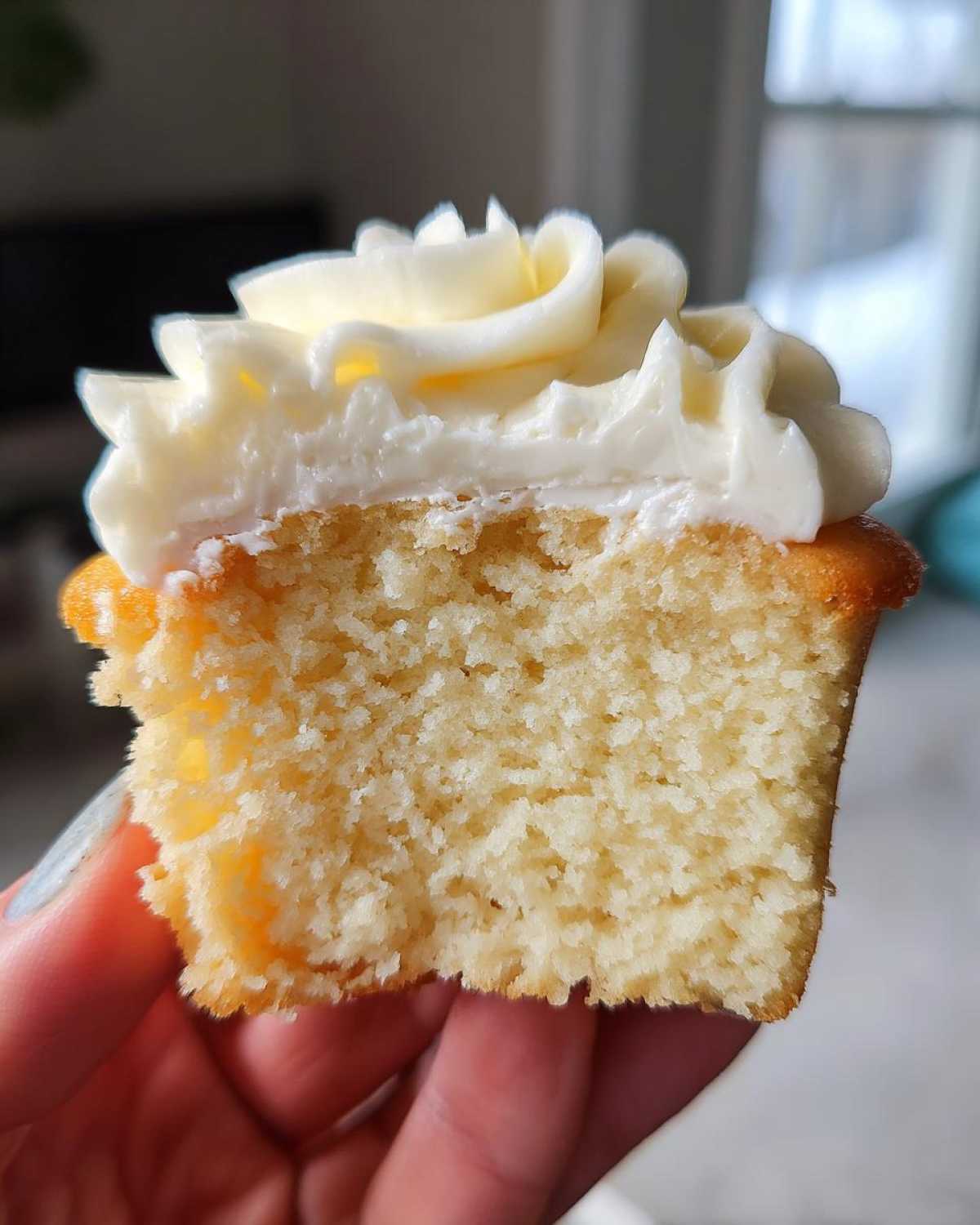 Close-up of a vanilla cupcake cut in half showing the fluffy, moist crumb and rich vanilla frosting swirl.