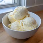 Close-up of four generous scoops of creamy vanilla protein ice cream in a white bowl.
