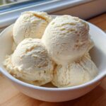 Four generous scoops of creamy, vanilla-colored protein ice cream served in a white bowl.