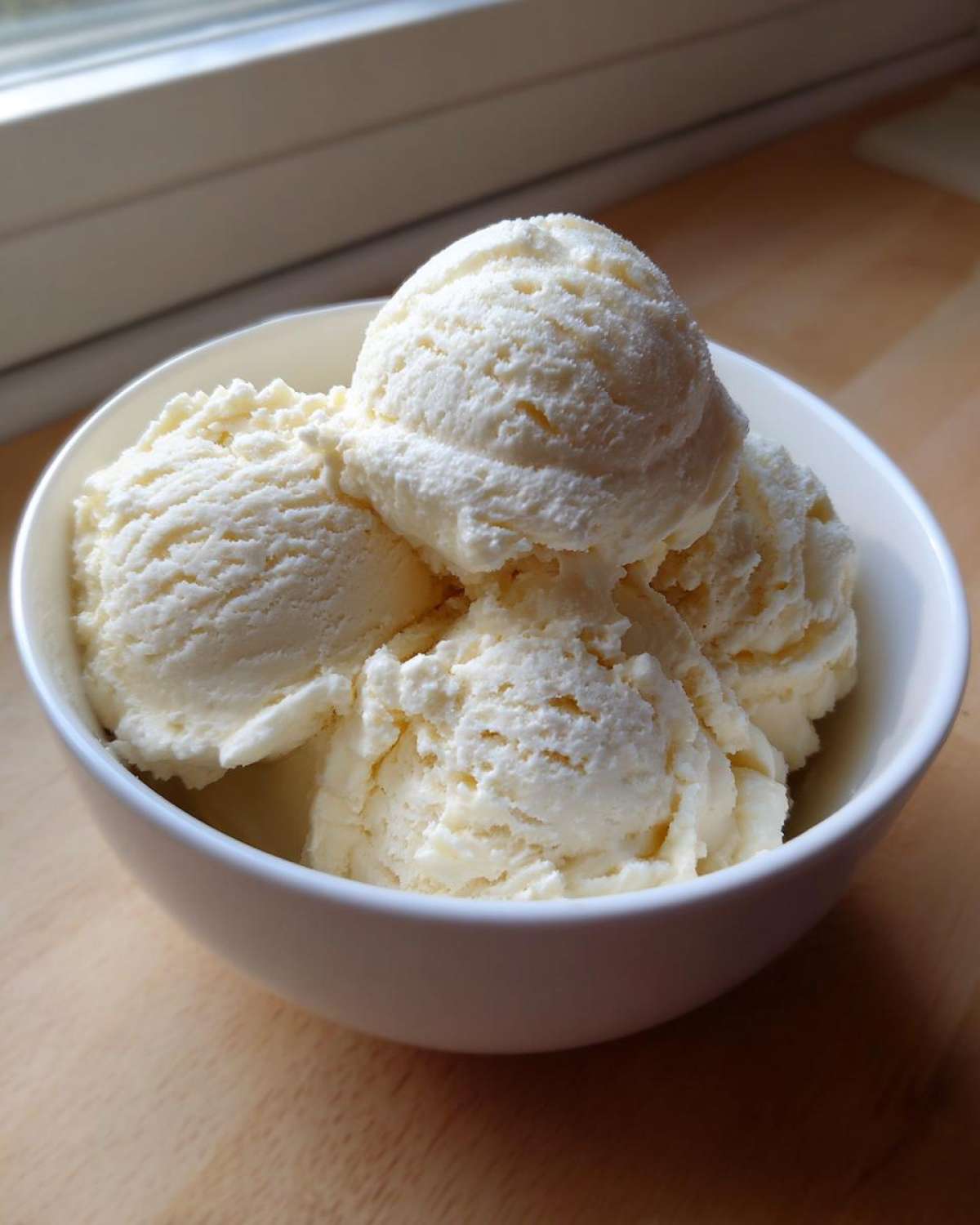 Four generous scoops of creamy, vanilla-colored protein ice cream served in a white bowl.