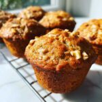 Close-up of golden brown banana nut muffins topped with chopped walnuts cooling on a wire rack.