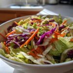 Close-up of a vibrant cabbage salad featuring shredded green and red cabbage and carrots in a white bowl.