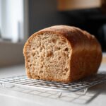 A loaf of freshly baked whole wheat bread, cut to show the soft crumb, resting on a wire cooling rack.