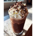A tall glass filled with rich frozen hot chocolate, topped high with whipped cream and dark chocolate shavings.