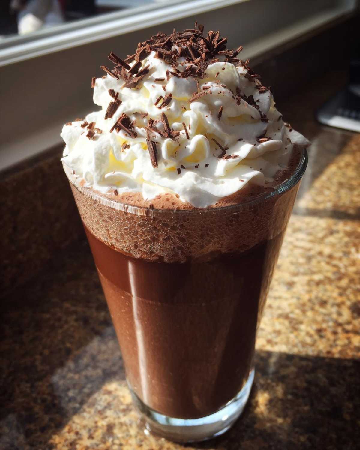 A tall glass filled with rich, blended frozen hot chocolate topped high with whipped cream and chocolate shavings.