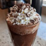 Close-up of a glass filled with blended frozen hot chocolate, topped high with whipped cream and chocolate shavings.