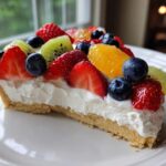 A slice of fruit pizza sugar cookie topped with cream cheese frosting and fresh berries and kiwi.