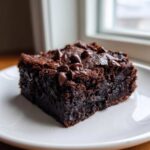 A close-up of a rich, fudgy black bean brownies square topped with chocolate chips on a white plate.