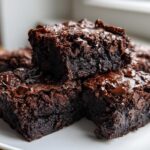 Close-up of fudgy, rich black bean brownies stacked on a white plate, topped with melted chocolate chips.