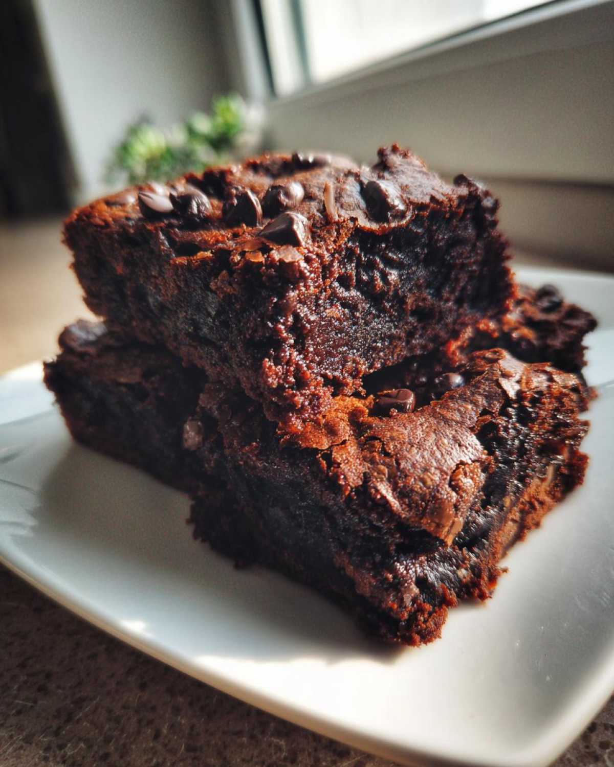Two stacked, fudgy black bean brownies topped with melted chocolate chips served on a white plate.