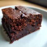 A close-up shot of a rich, dark, fudgy sweet potato brownies square on a light plate.