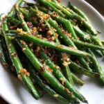 Close-up of vibrant, glossy green beans tossed with crispy browned garlic pieces.