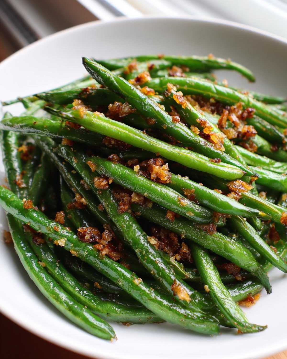 Close-up of vibrant green beans tossed with crispy, browned garlic bits, ready to serve.