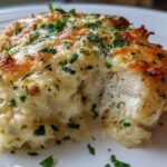 Close-up of a moist Garlic parmesan chicken bake, cut open to show white meat covered in melted, browned cheese and fresh parsley.