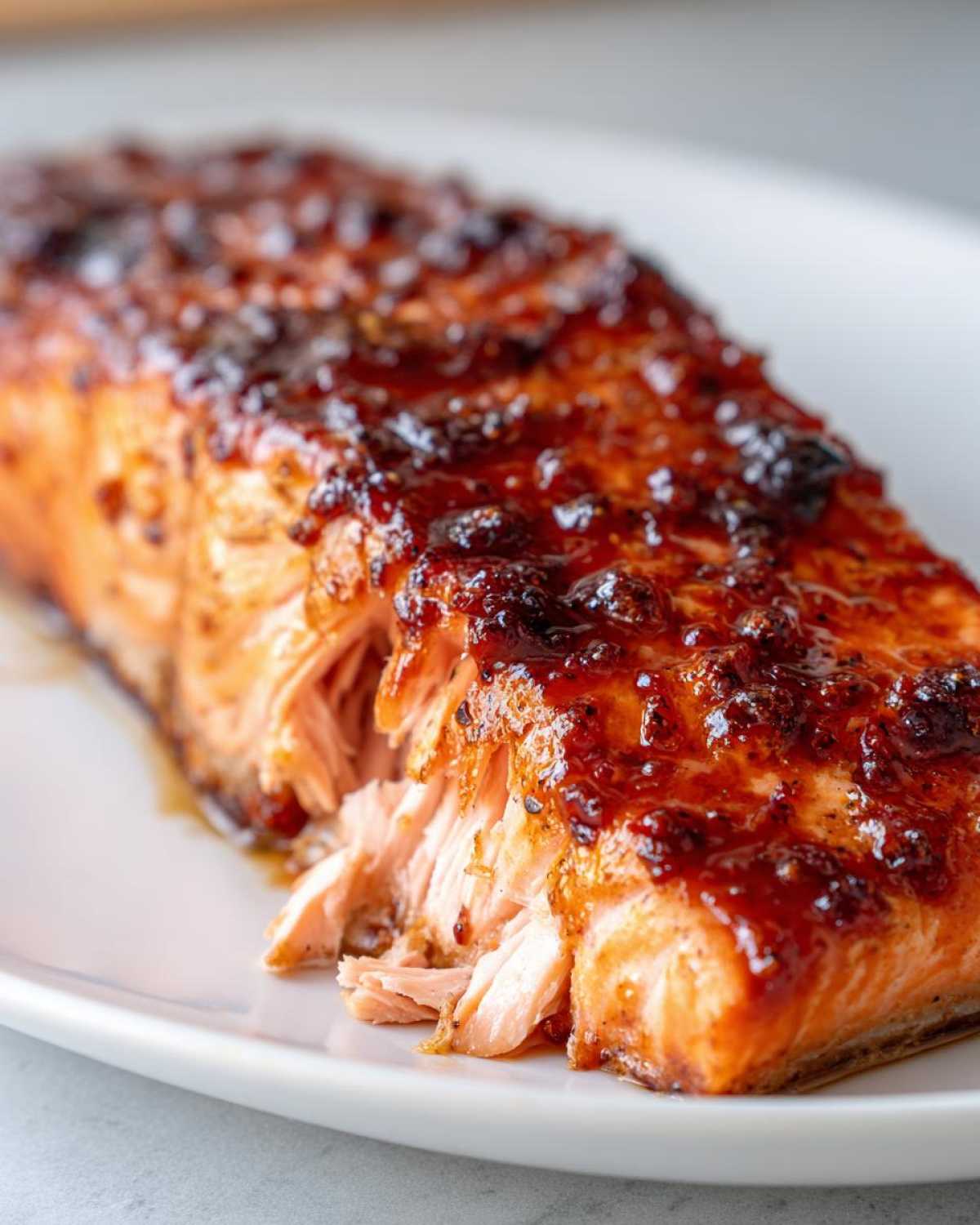 Close-up of a perfectly cooked, glazed salmon fillet showing flaky texture on a white plate.